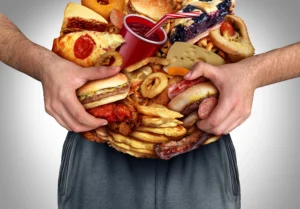 erectile dysfunction. Person holding a large pile of fast food items, including burgers, pizza, fries, fried chicken, onion rings, and a soft drink.