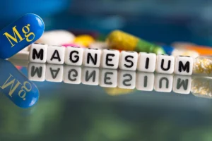 Magnesium. Pills and letter blocks spell out "MAGNESIUM," with a blue capsule marked "Mg" on a reflective surface.