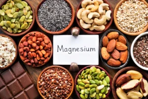 Magnesium. Various foods high in magnesium including seeds, nuts, legumes, and dark chocolate surround a card labeled "Magnesium.