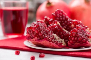 Natural foods. A plate with pomegranate seeds, a whole pomegranate, and a glass of pomegranate juice on a red napkin.