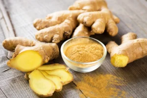 Natural foods. Whole ginger roots, ginger slices, and a small glass bowl filled with ground ginger powder are arranged on a wooden surface.