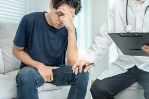 masturbation. A man sits with his head in his hand looking distressed, while a doctor with a clipboard rests a comforting hand on his knee during a consultation.