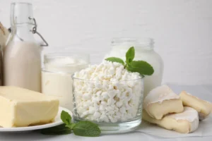 Natural foods. A variety of dairy products including butter, cottage cheese, yogurt, milk, and soft cheese are arranged on a white surface, with mint leaves used as garnish.