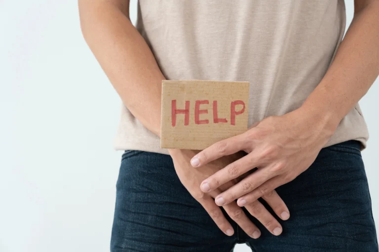 Premature ejaculation. A person stands with hands covering their crotch, holding a cardboard sign that says "HELP" in red letters.
