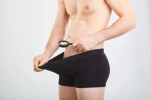 testosterone. Shirtless man wearing black underwear uses a magnifying glass to look inside his waistband.